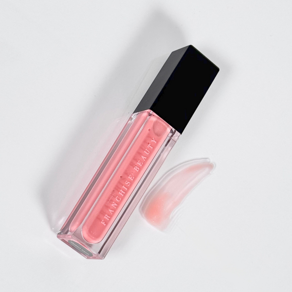 Close-up of Franchise Beauty’s Desert Sand lip gloss with gold shimmer in a clear, eco-friendly tube.

