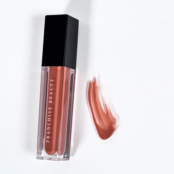 Franchise Beauty Dusted Clay lip gloss in a pigmented brick brown shade, shown in sleek, recyclable packaging