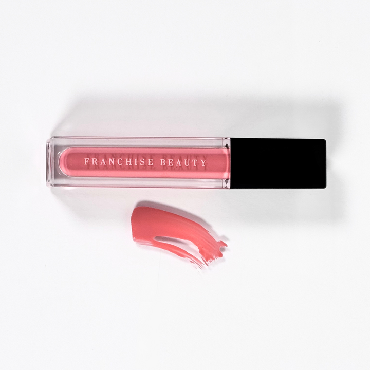 Franchise Beauty Lantana lip gloss, in sleek recyclable packaging showing a rich coral color with a non-sticky, high-shine texture.