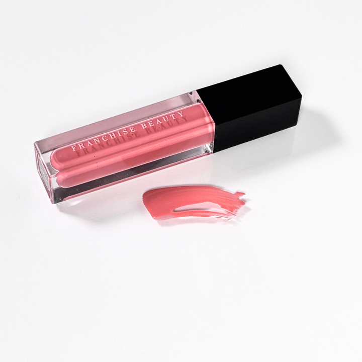 Franchise Beauty Lantana lip gloss, in sleek recyclable packaging showing a rich coral color with a non-sticky, high-shine texture.