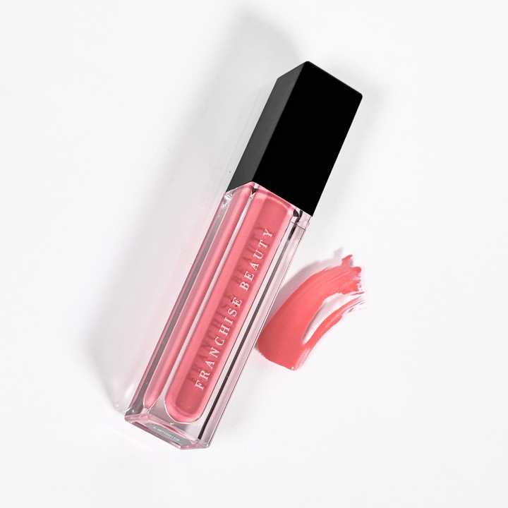 Franchise Beauty Lantana lip gloss, in sleek recyclable packaging showing a rich coral color with a non-sticky, high-shine texture.