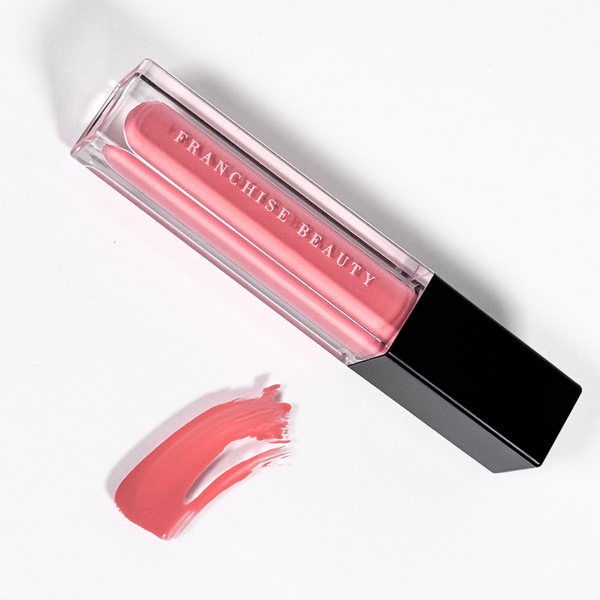 Franchise Beauty Lantana lip gloss, in sleek recyclable packaging showing a rich coral color with a non-sticky, high-shine texture.