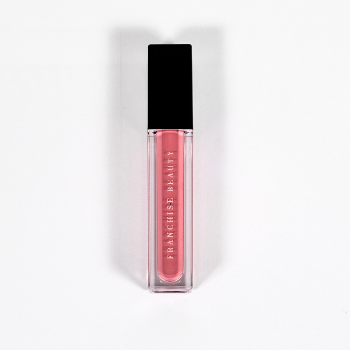 Franchise Beauty Lantana lip gloss, in sleek recyclable packaging showing a rich coral color with a non-sticky, high-shine texture.