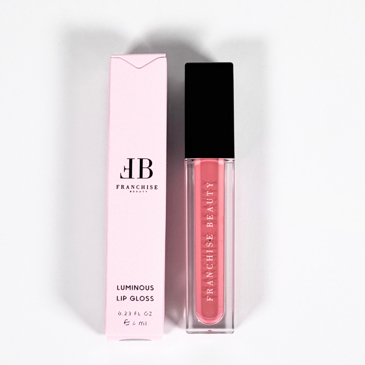 Franchise Beauty Lantana lip gloss, in sleek recyclable packaging showing a rich coral color with a non-sticky, high-shine texture.